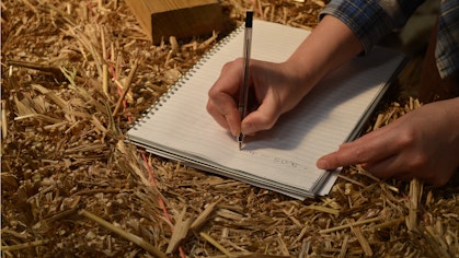 Student writing notes on top of a straw bale
