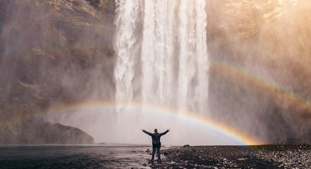 man standing by waterfall and rainbow