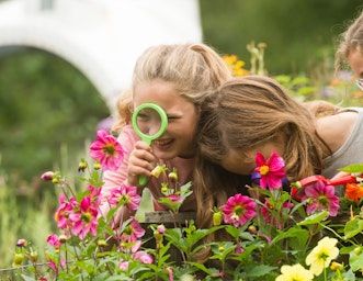 Kids surrounded by flowers looking through a magnifying glass