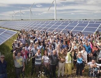 People involved in the Westmill Solar Farm community energy project standing in front of PV solar panels and wind turbines