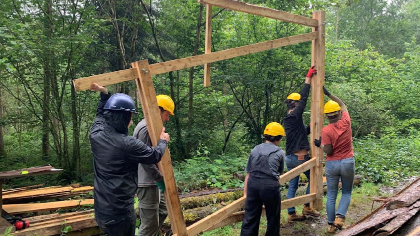 CAT Architecture students move a partially constructed timber frame around in a wooded area